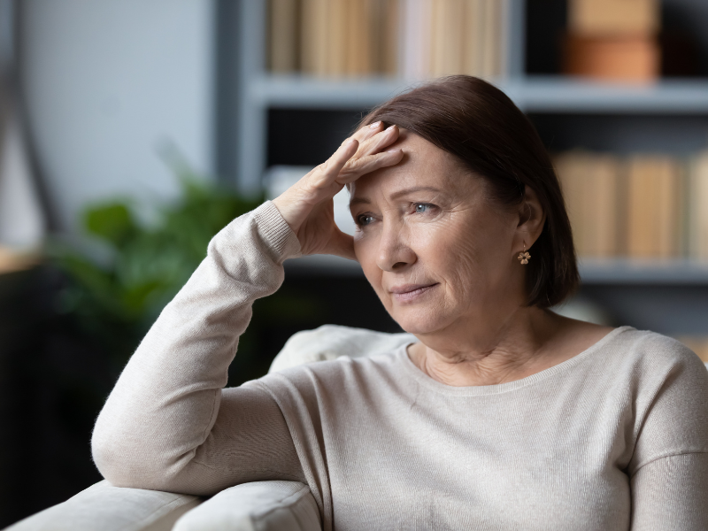 Frau 40+ sitzt auf Sofa und schaut betrübt und nachdenklich